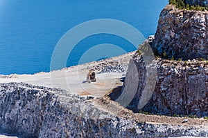 Aerial view of opencast mining quarry with one machinery on the blue sea background.