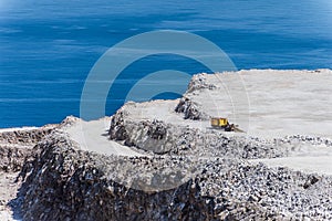 Aerial view of opencast mining quarry with one machinery on the blue sea background.