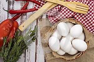 Aerial view of organic farm white eggs in a basket on a rustic wooden table with chili peppers and rosemary