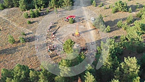 Aerial view of the organized gathering of people near a large campfire in a pine forest