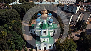 Aerial view of an orthodox church with domes and a bell tower in a city block surrounded by trees on a summer day
