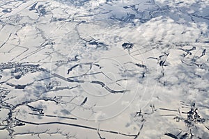 Aerial view over clouds top to snow covered rivers, fields and roads, winter fresh frosty air