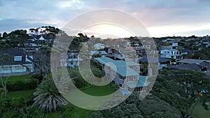 Aerial view over the shore and rooves of seaside houses at Murrays bay, Auckland, during the sunset