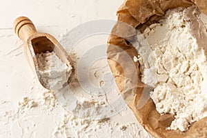 Aerial view of paper bag with flour and wooden spoon on wooden table with flour, horizontal,
