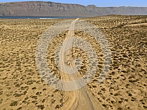 Aerial view of people cycling on a dirt path in the island of La Graciosa, Lanzarote, Canary Islands. Spain.