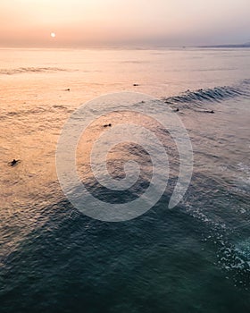 Aerial view of people waiting for waves to surf at sunset in Atlantic Ocean open water off Costa da Caparica coastline, Setubal,