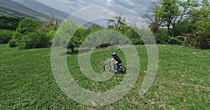 Aerial view person rider sports mountain bike downhill speed movement on green grass slope at cliff