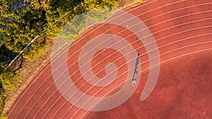 Aerial view of a person running on a running track with the sun casting a golden light on the path