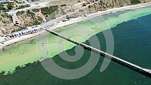 Aerial view of a pier over a crystal-clear green sea under shade from the bright sunlight