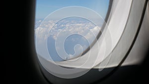 Aerial view through plane window with view over puffy white cloud with clear blue sky while flying, View from the window of the