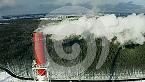 Aerial view of a polluting industrial smokestack on forest background in winter