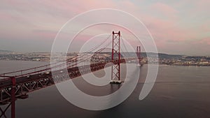 Aerial view of Ponte 25 de Abril bridge in Lisbon, Portugal, with pink cloudy sky in the background