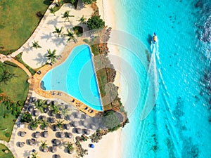 Aerial view of pool, sandy beach, palms, umbrellas, boat, sea