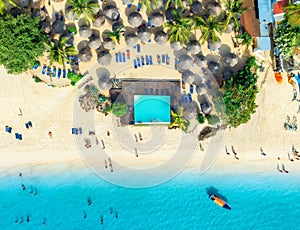 Aerial view of pool, sandy beach, palms, umbrellas, boat, sea