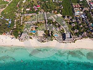 Aerial view of pool, umbrellas, sandy beach with green Palm trees. Coast of Indian ocean at sunset in summer. Zanzibar