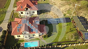 Aerial view of a private house with green grass covered yard, solar panels on roof, swimming pool with blue water and wind turbine