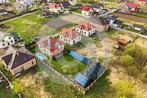 Aerial view of a private house with green grass covered yard, solar panels on roof, swimming pool with blue water and wind turbine