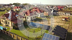 Aerial view of a private house with green grass covered yard, solar panels on roof, swimming pool with blue water and wind turbine