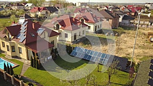 Aerial view of a private house with green grass covered yard, solar panels on roof, swimming pool with blue water and wind turbine