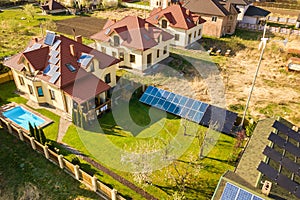 Aerial view of a private house with green grass covered yard, solar panels on roof, swimming pool with blue water and wind turbine