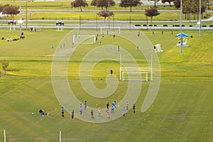 Aerial view of public sports park with children engaged in football game on grass stadium at sunset. Active way of life