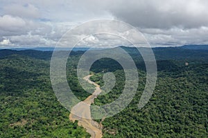 Aerial view of the rainforest with a large brown river meandering through the landscape and shadows of clouds over the rainforest