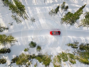 Aerial view of red car driving through the white snow winter forest on country road in Finland, Lapland