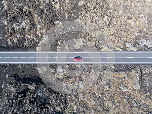 Aerial view of a red car on a road that runs through lava fields of Lanzarote, Canary Islands, Spain