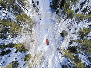 Aerial view of a red car on white winter road. Winter landscape countryside. Aerial photography of snowy forest with a car on the