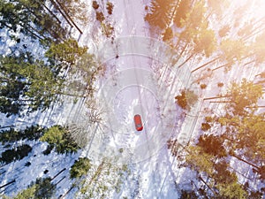 Aerial view of a red car on white winter road. Winter landscape countryside. Aerial photography of snowy forest with a red car on