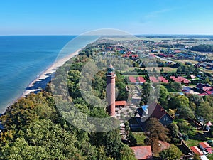 Aerial view at red lighthouse, at baltic sea coast with forest and buildings.