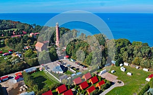 Aerial view at red lighthouse, at baltic sea coast with forest and buildings.