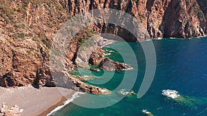 Aerial view of red rock cliffs mountain, sand beach, waves crushing on the beach. Colored sea, blue turquoise, high red