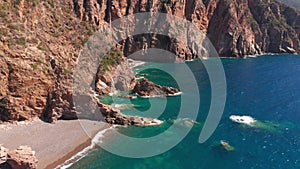 Aerial view of red rock cliffs mountain, sand beach, waves crushing on the beach. Colored sea, blue turquoise, high red