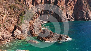 Aerial view of red rock cliffs mountain, sand beach, waves crushing on the beach. Colored sea, blue turquoise, high red