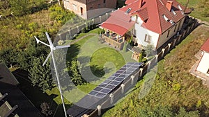 Aerial view of a residential private house with solar panels on roof and wind generator turbine.