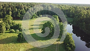 Aerial view of river in green meadows, beautiful sunset light. Evening panorama. Birch trees on riverbank