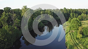 Aerial view of river in green meadows, beautiful sunset light. Evening panorama. Birch trees on riverbank