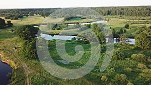 Aerial view of river in green meadows, beautiful sunset light. Evening panorama. Birch trees on riverbank