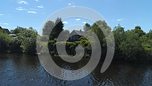 Aerial view of a river in summer village and an old wooden house. Shot. Forest and small house surrounded by green trees