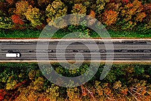 Aerial view of road and a car in autumn forest with red, yellow and orange leaves