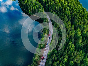 Aerial view of road with cars between green forest and blue lake water in Finland