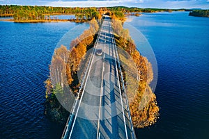 Aerial view of road and forest in autumn colors with blue water lake