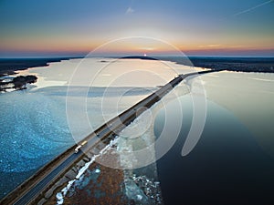 Aerial view of road in the frozen lake with moving cars on sunset.