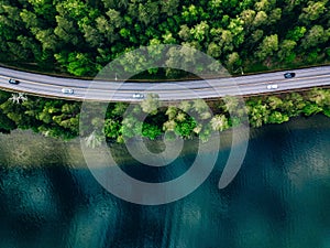 Aerial view of road between green forest and blue lake in Finland