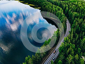 Aerial view of road between green forest and blue lake in Finland