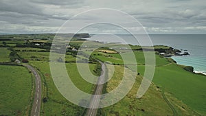 Aerial view road green meadows panning up. Car drives along farmland way in Irish coutryside