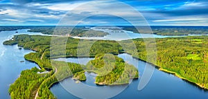 Aerial view of road between green summer forest and blue lake in Finland