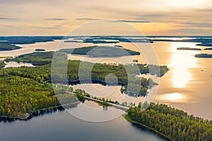 Aerial view of road between green summer forest and blue lake in Finland. Summer sunset lanscape