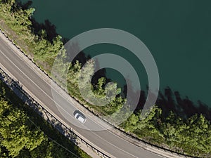Aerial view of road between green summer forest and lake